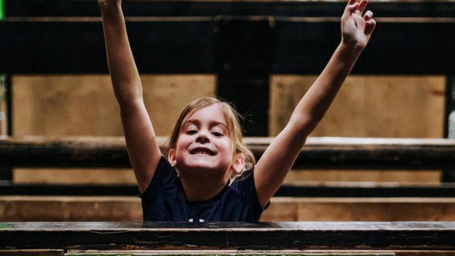 A young girl celebrates after getting over a wall obstacle.